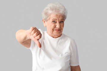 Displeased senior woman showing thumb-down on grey background