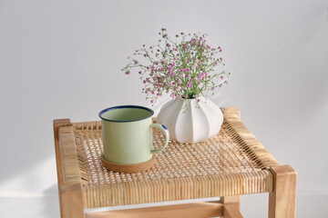Mug and vase with flowers on wicker table