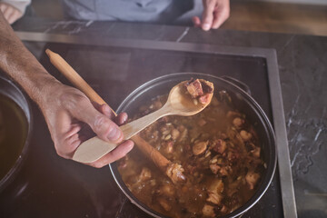 Crop man cooking stewed meat in saucepan