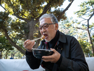 An older asian man eating noodles and soup with chopsticks - 629243765