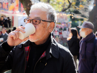 An older asian man drinking coffee outside