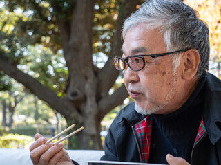 An older asian man eating noodles and soup with chopsticks - 629244184