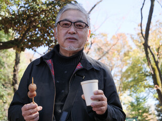 An older Japanese man eating dango and drinking coffee
