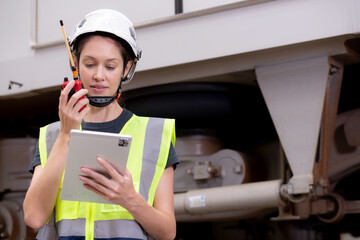 Young caucasian engineer woman using radio for command with worker checking electric train for planning maintenance and looking digital tablet in station, inspector check transport and infrastructure.