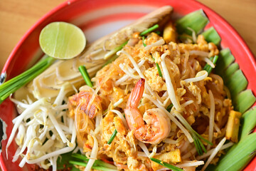 Pad Thai is placed on a brown wooden table. There is a woman squeezing lime juice to add more seasoning. Because Thai people like to eat spicy food. Famous Thai food concept. Street food. Thai identit