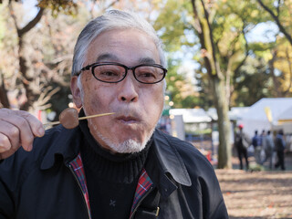 An asian man in glasses eating dango