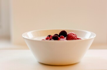 White bowl with a creamy yogurt base filled with vibrant red raspberries and granola