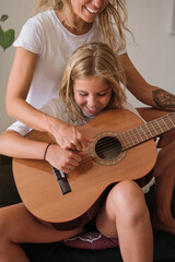 Blonde girl playing guitar while smiling with a woman sitting with her