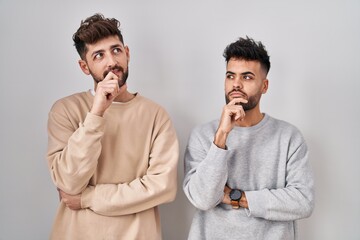 Young homosexual couple standing over white background with hand on chin thinking about question, pensive expression. smiling and thoughtful face. doubt concept.