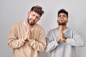 Young homosexual couple standing over white background begging and praying with hands together with...