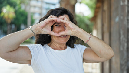 Middle age hispanic woman smiling confident doing heart gesture with hands at park
