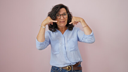 Middle age hispanic woman smiling confident doing telephone gesture with hand over isolated pink background