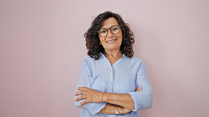Middle age hispanic woman wearing glasses standing with crossed arms over isolated pink background