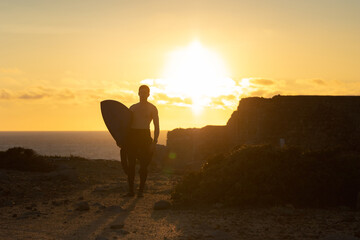 Fit man with naked torso standing nearby ocean at bright sunset