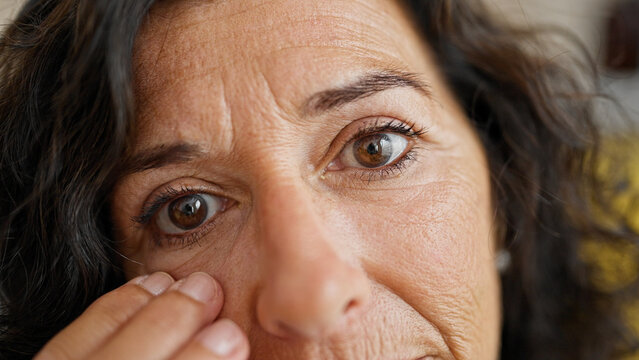 Middle age hispanic woman touching baggy eyes at home