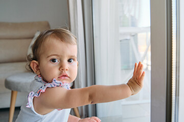 Curious toddler touching window and looking at camera