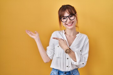 Young beautiful woman wearing casual shirt over yellow background amazed and smiling to the camera while presenting with hand and pointing with finger.