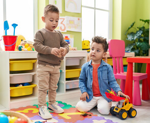 Adorable boys playing with tractor and dinosaur toy sitting on floor at kindergarten