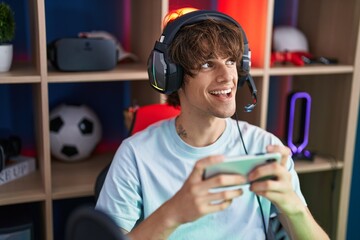 Young blond man streamer playing video game using smartphone at gaming room