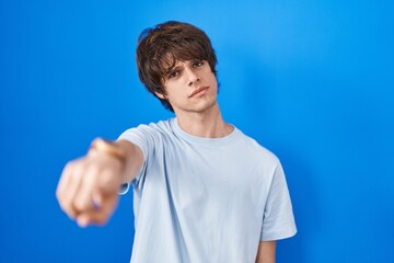 Hispanic young man standing over blue background pointing displeased and frustrated to the camera,...