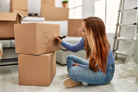Young caucasian woman writing books word on cardboard box at new home