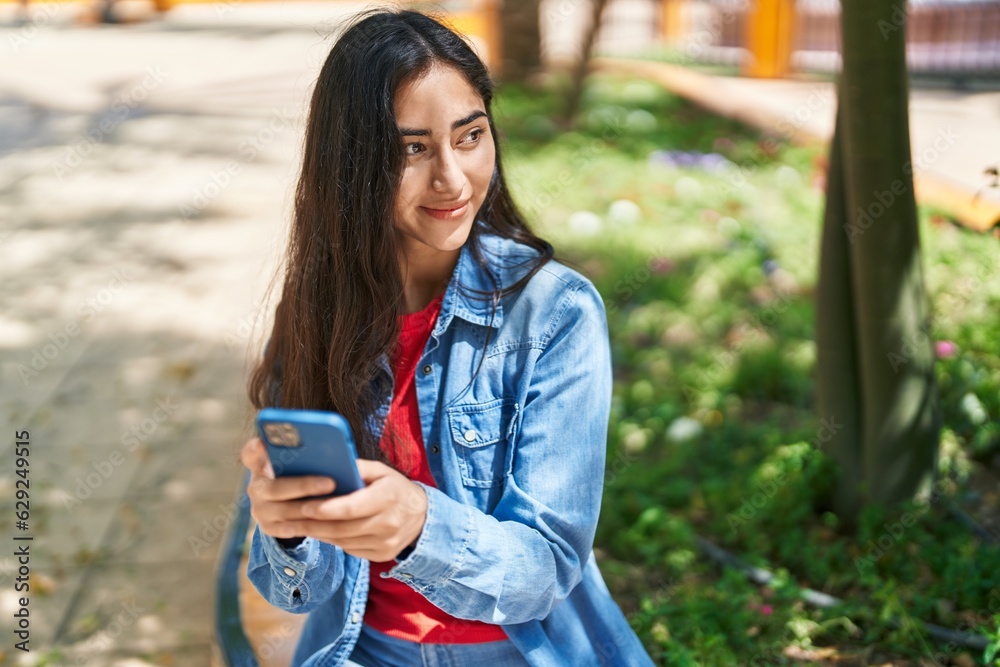 Wall mural Young hispanic girl smiling confident using smartphone at park