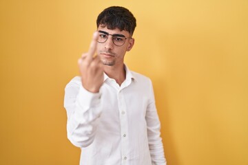 Young hispanic man standing over yellow background showing middle finger, impolite and rude fuck...