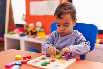 Adorable hispanic boy playing with maths puzzle game sitting on table at kindergarten