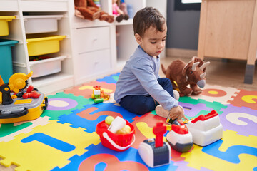 Adorable hispanic boy playing supermarket game sitting on floor at kindergarten