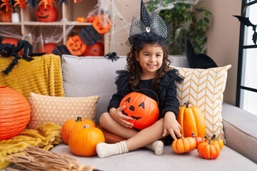 Adorable hispanic girl having halloween party holding pumpkin basket at home