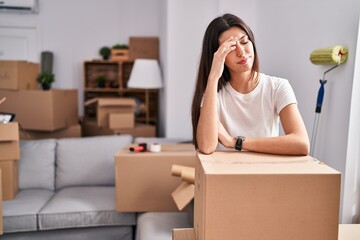 Young beautiful hispanic woman leaning on package with worried expression at new home