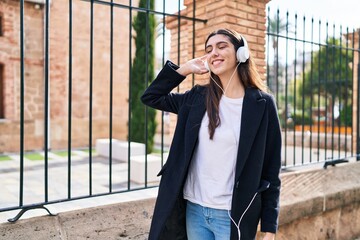Fototapeta premium Young beautiful hispanic woman listening to music standing at street