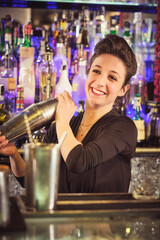Positive female barkeeper shaking cocktail in bar