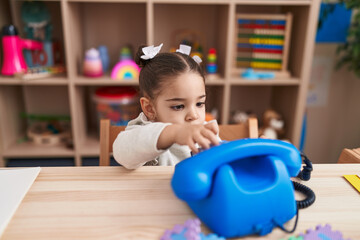 Adorable hispanic girl playing telephone toy sitting on table at kindergarten