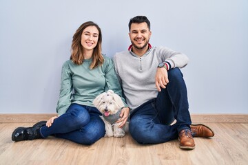Young hispanic couple sitting on the floor with dog with a happy and cool smile on face. lucky...