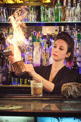 Concentrated female barkeeper making flame while mixing cocktail