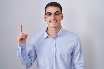 Handsome hispanic man wearing business clothes and glasses pointing finger up with successful idea. exited and happy. number one.