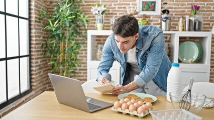 Young hispanic man writing on notebook online recipe at dinning room