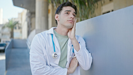 Young hispanic man doctor stressed standing at hospital