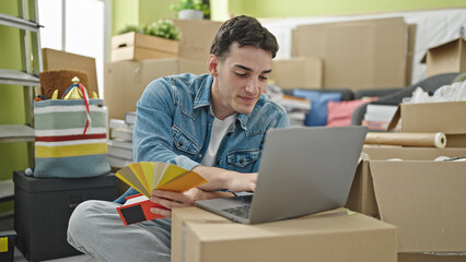 Young hispanic man using laptop choosing color paint at new home