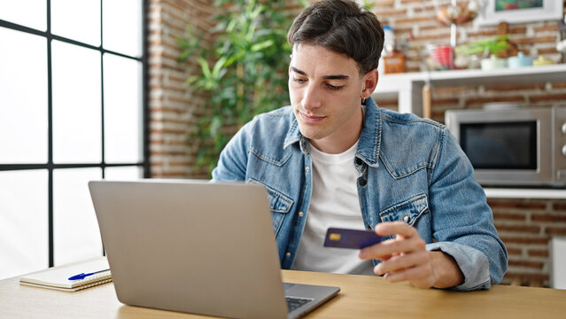 Young hispanic man shopping with laptop and credit card sitting on table at dinning room
