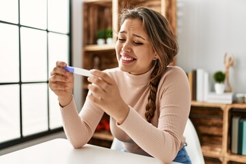 Young beautiful hispanic woman smiling confident holding pregnancy test at home - obrazy, fototapety, plakaty