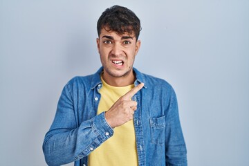 Young hispanic man standing over blue background pointing aside worried and nervous with...