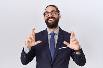 Hispanic man with beard wearing suit and tie gesturing finger crossed smiling with hope and eyes closed. luck and superstitious concept.
