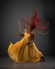 African American female in a long, yellow dress displaying an energetic dance performance
