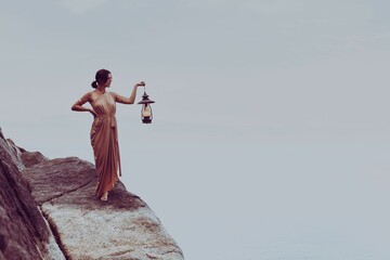 Mature woman stands on the side of a mountain, with an antique lantern holding in her hands