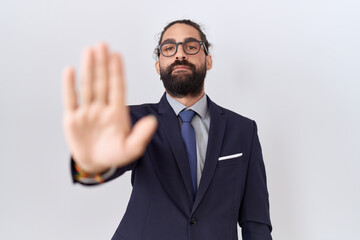 Hispanic man with beard wearing suit and tie doing stop sing with palm of the hand. warning expression with negative and serious gesture on the face.