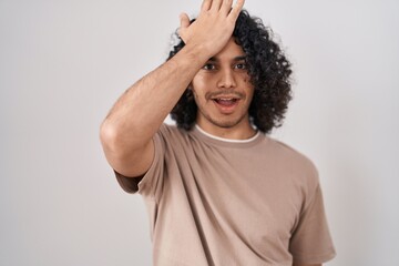 Fototapeta na wymiar Hispanic man with curly hair standing over white background surprised with hand on head for mistake, remember error. forgot, bad memory concept.