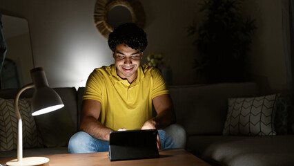 Young latin man using touchpad sitting on sofa at home