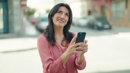 Middle age hispanic woman smiling confident using smartphone at street